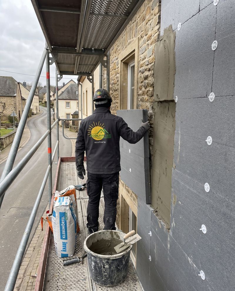 Ouvrier Ecolive Lux posant des panneaux isolants sur une façade depuis un échafaudage