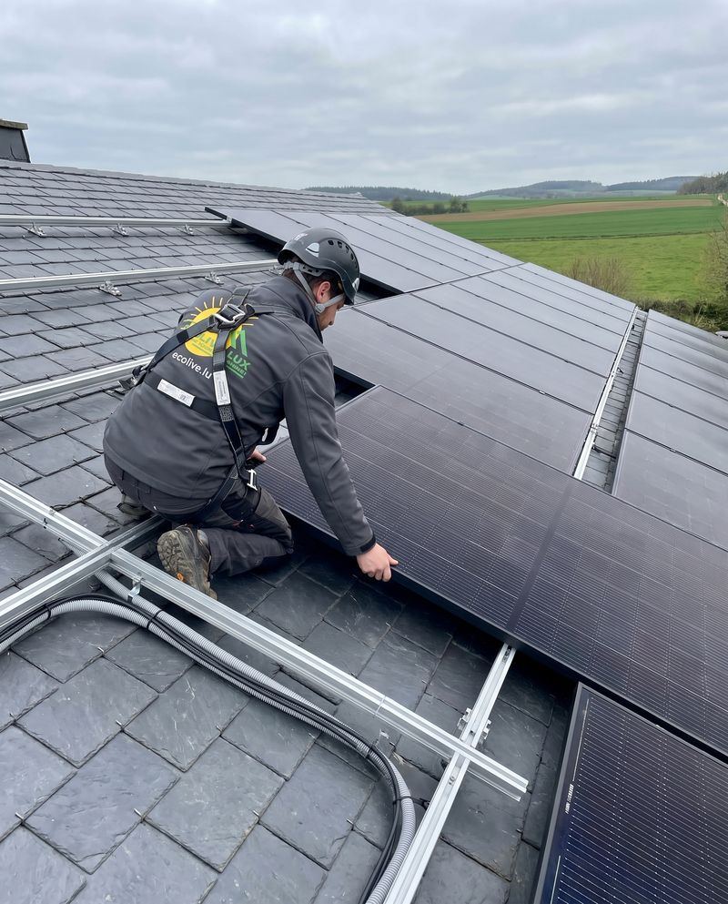 Installateur Ecolive Lux glissant un panneau photovoltaïque sur les rails d'une toiture en ardoise